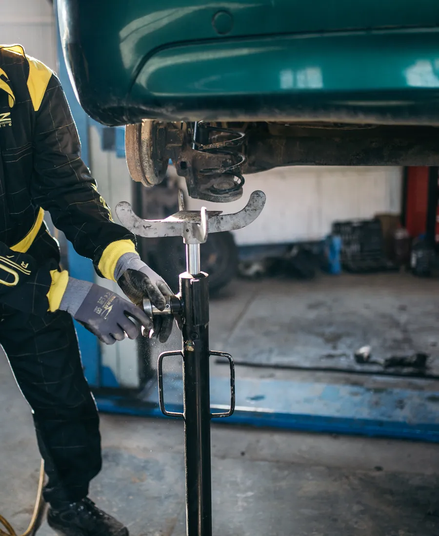 Close crop of a technician setting a jack beneath a raised vehicle