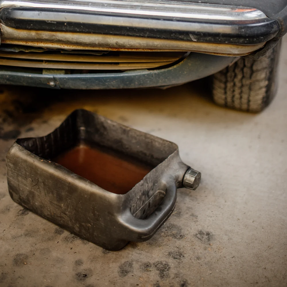 Engine oil draining into a catch pan under a vehicle
