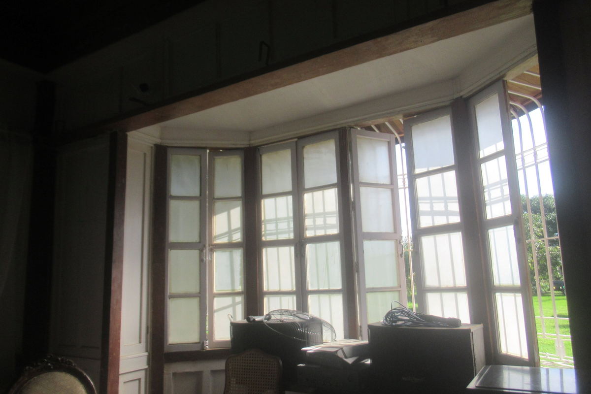 A wide period room with tall shuttered windows, a patterned floor and dark timber furniture set against pale walls.