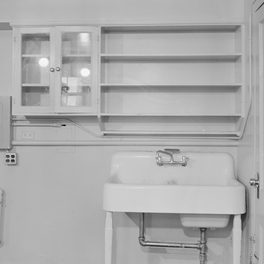 Office detail: a glazed kitchen cupboard and a run of open shelves above a deep sink.