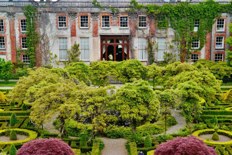 A large stone house seen from the garden side, with lawns and planting running up to the front of it.