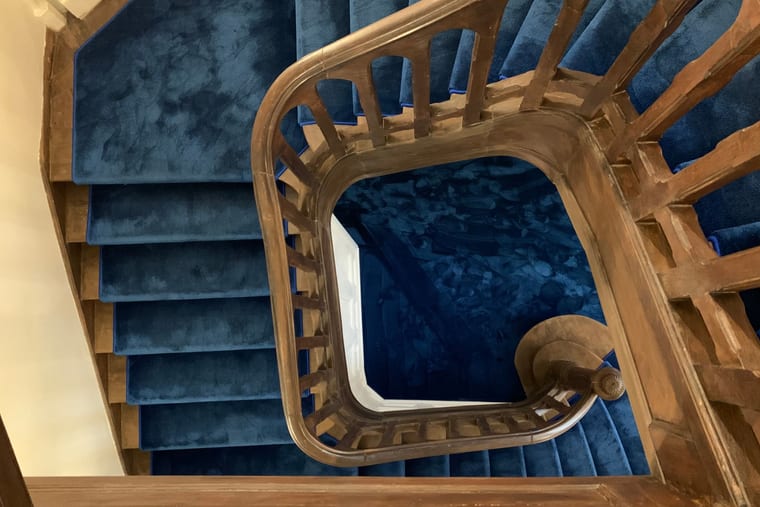 A stairwell seen from above, its timber balustrade winding around the well over deep blue carpet.