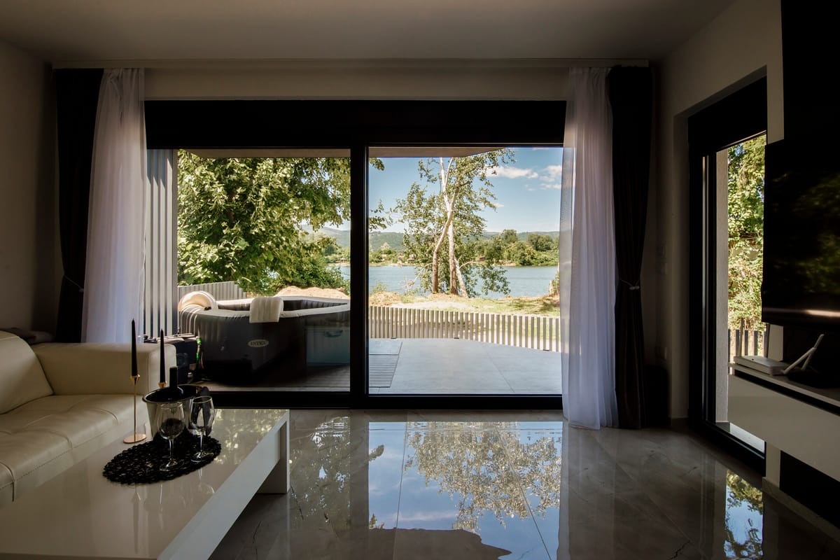 A living room with floor-to-ceiling windows opening onto a view of trees and water.