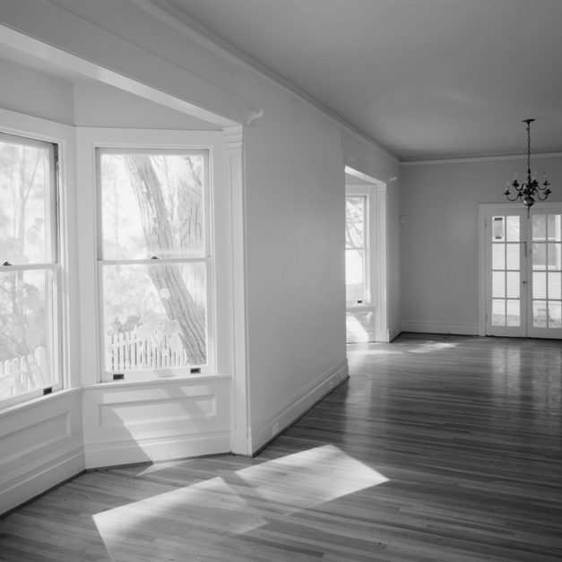 An empty living room with a wide bay window, panelled walls and polished floorboards.
