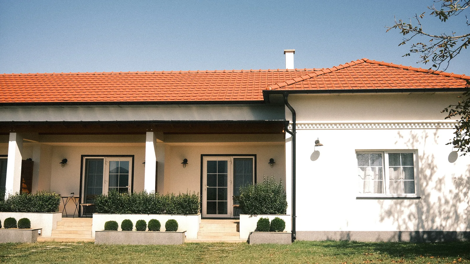 Single-storey white house with a terracotta tile roof seen from the street