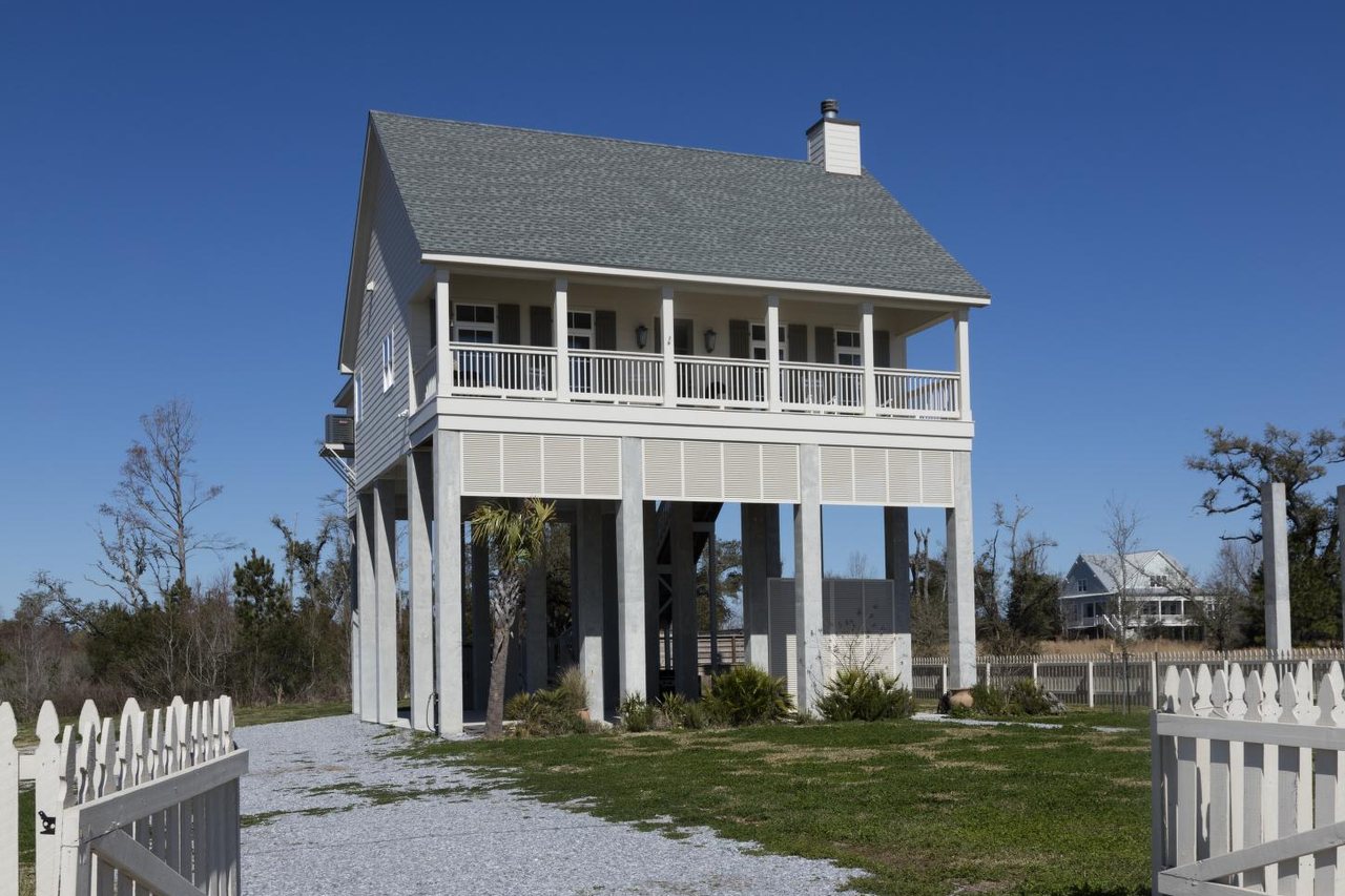 A newly built raised coastal house with a deep front porch and a white picket fence
