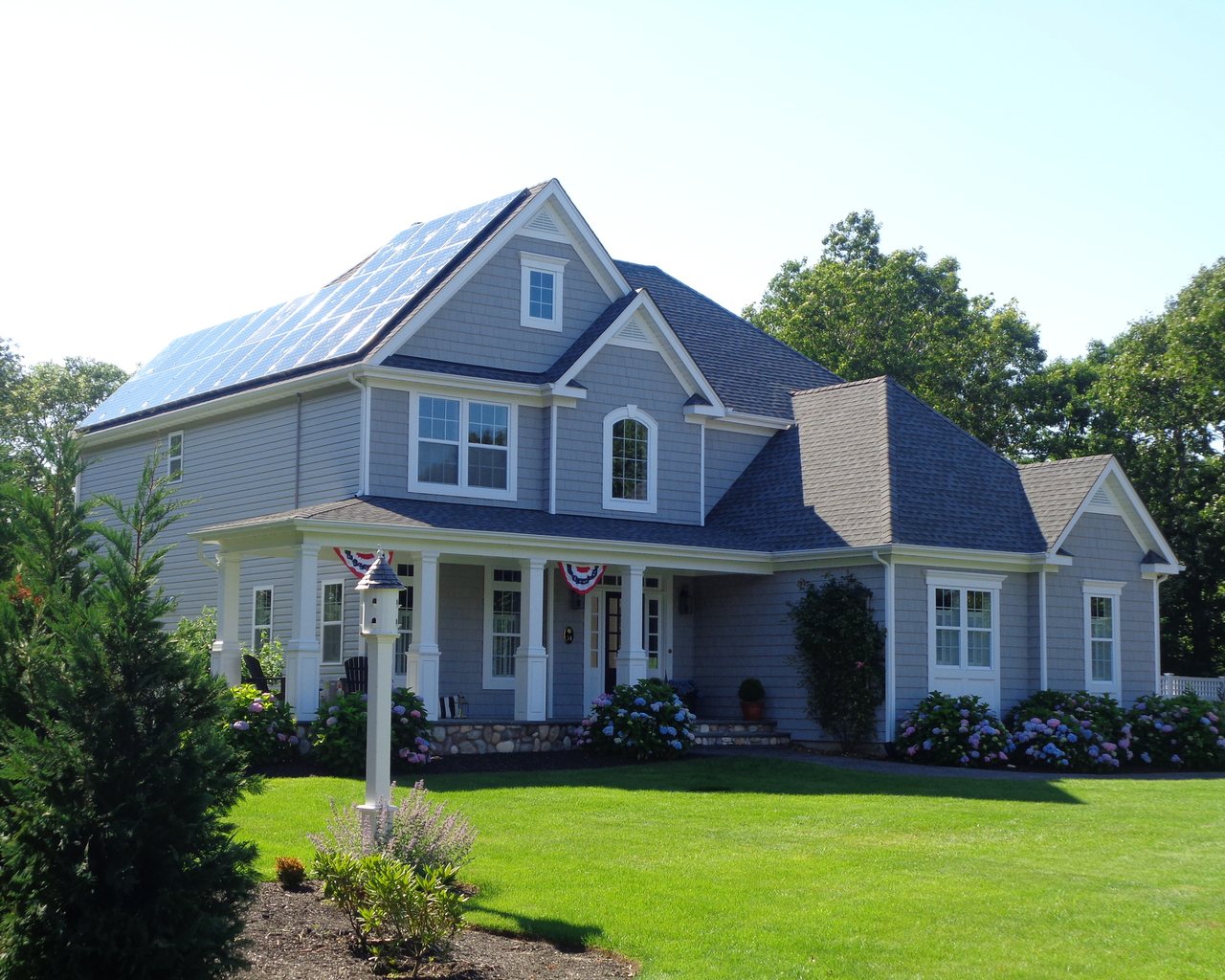 A two-storey suburban home with a full roof solar array above a green front lawn