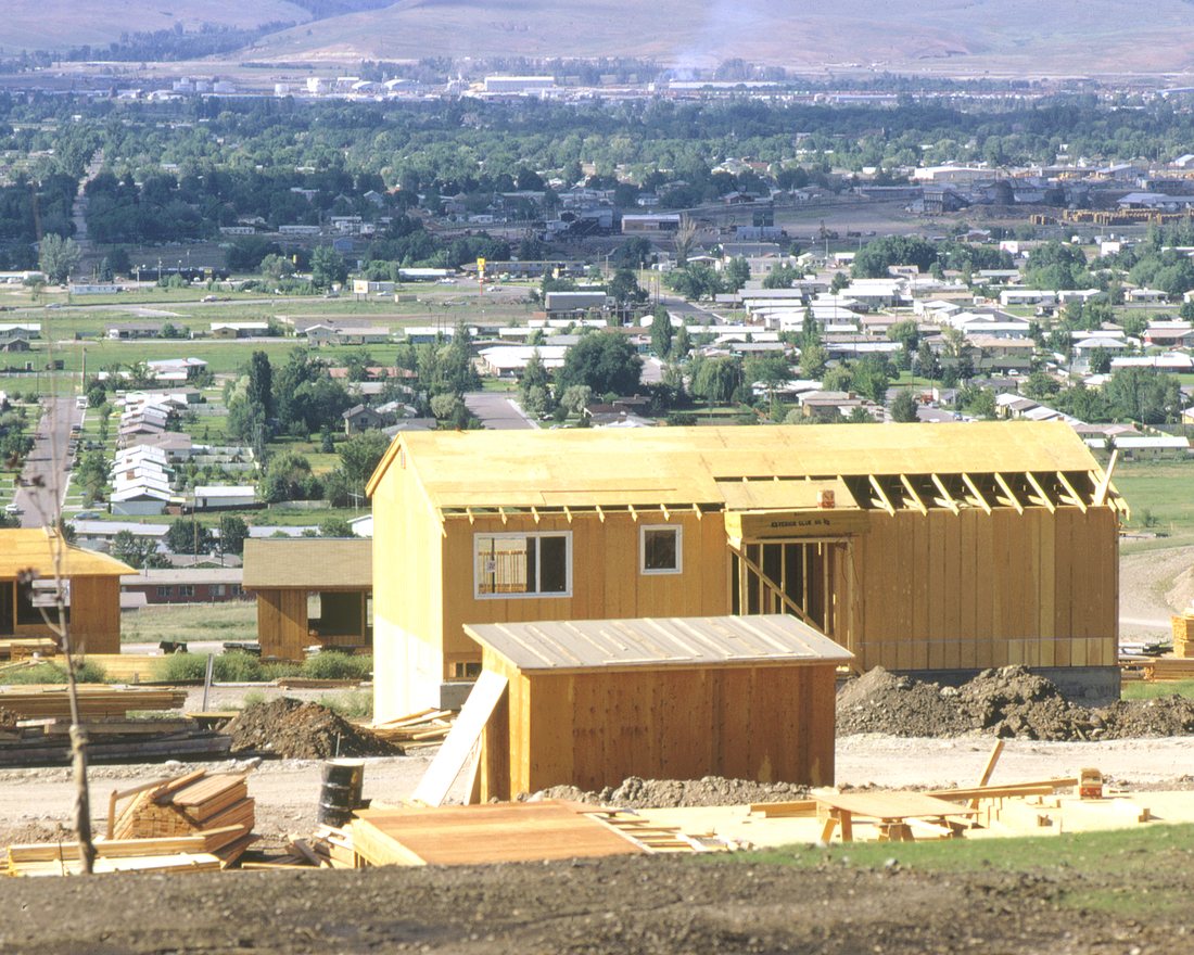 Timber-framed new houses under construction above a wide green valley