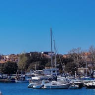 The foot of a white sail above a harbour of moored boats.