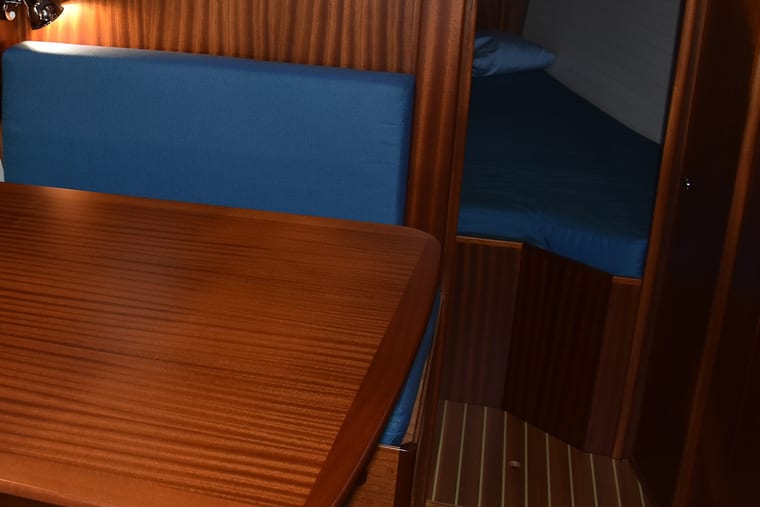 A saloon berth with blue cushions and varnished joinery below deck.