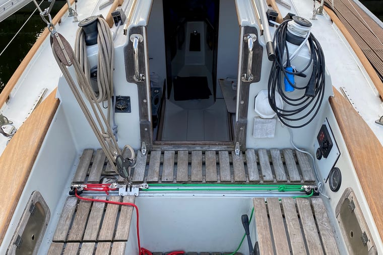 Looking down into the cockpit of a small sailing yacht: slatted wooden gratings, an open companionway and coiled lines stowed on the coaming.