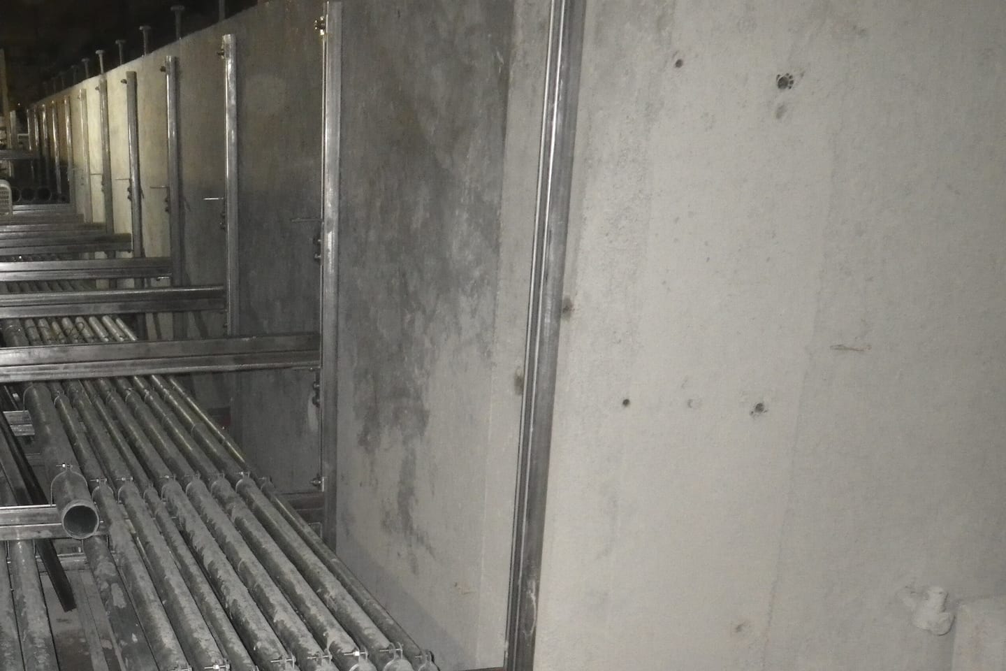 Steel conduits stacked on racking inside a narrow concrete service void.