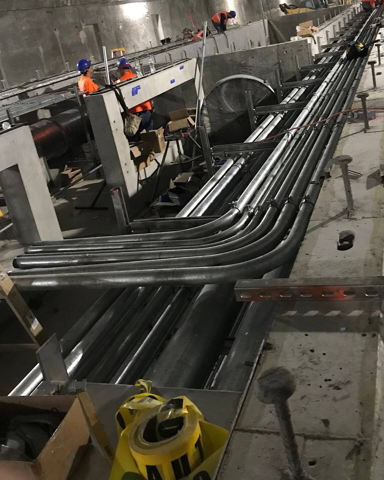 Conduits curving along a service corridor on a working site, with figures working at a distance.