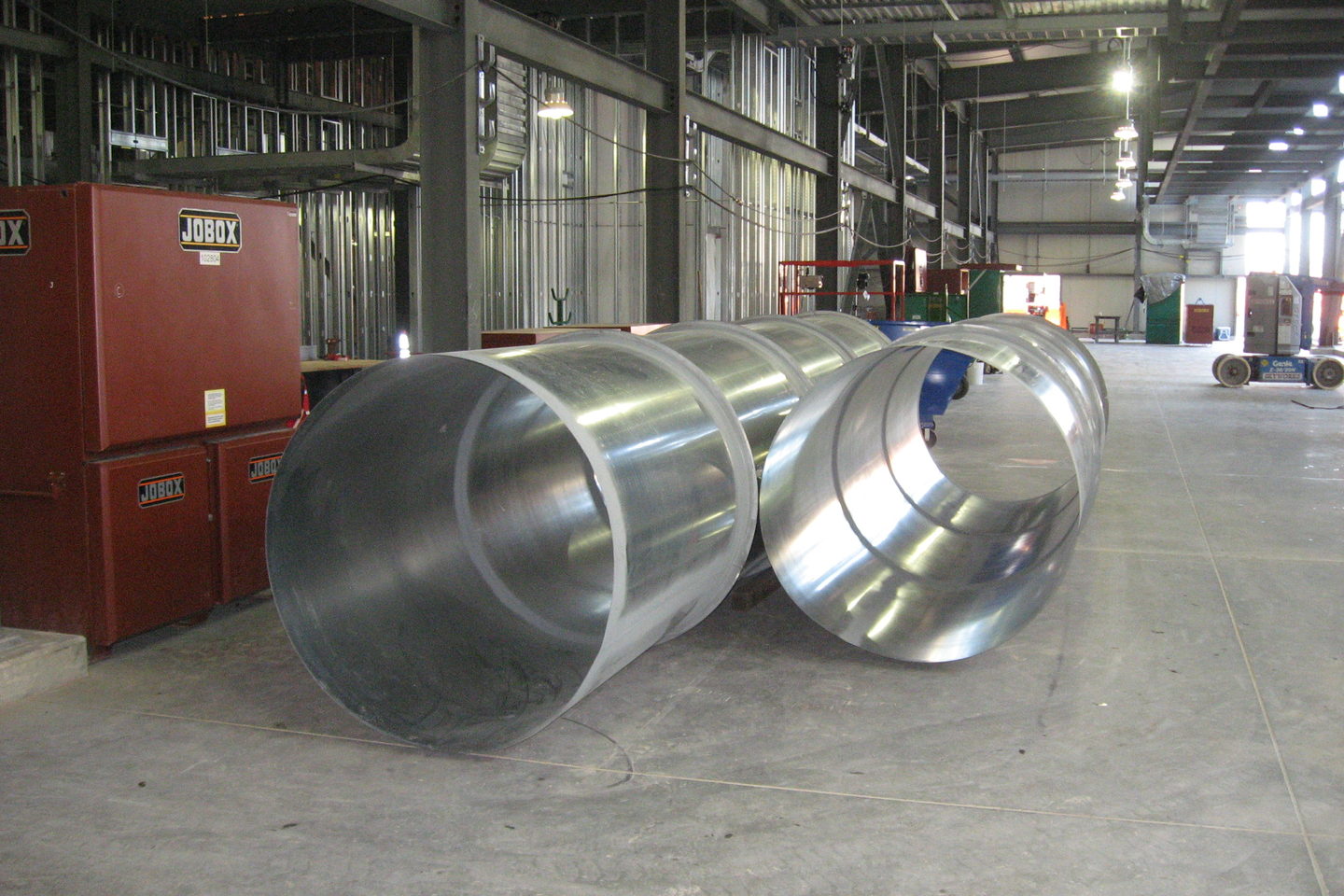 A plant room interior with large pale ducting overhead and insulated pipework along the wall.