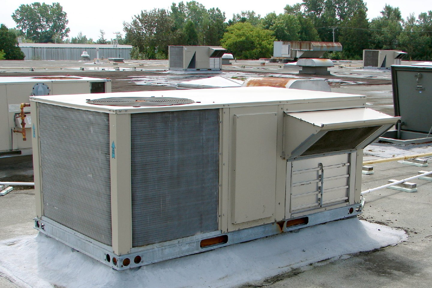 Two packaged rooftop units side by side on a flat roof, their duct connections dropping through the deck.