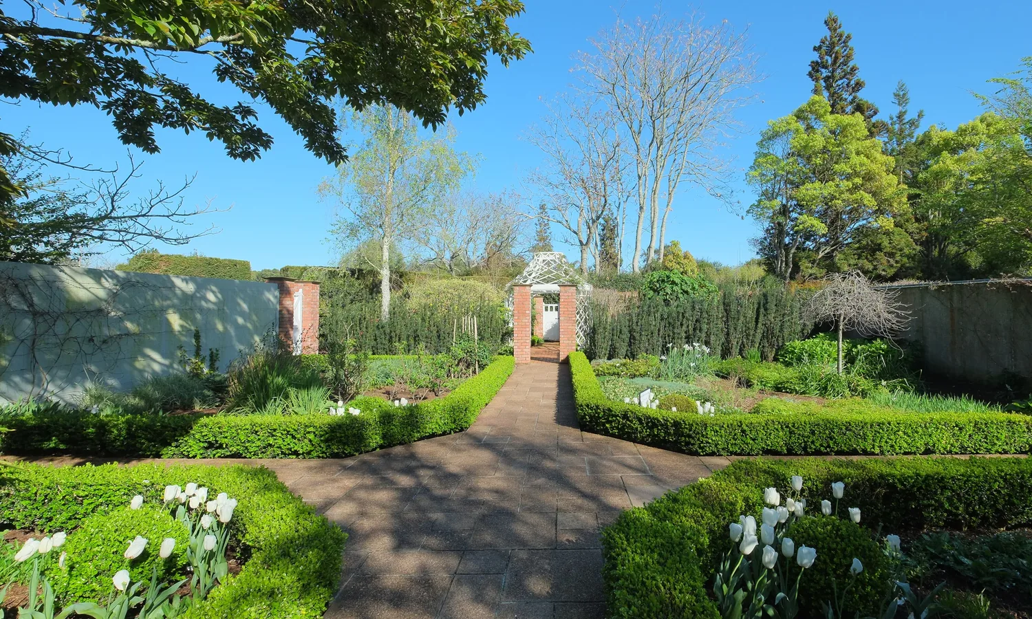 Brick garden doorway at the end of a gravel path between clipped box beds