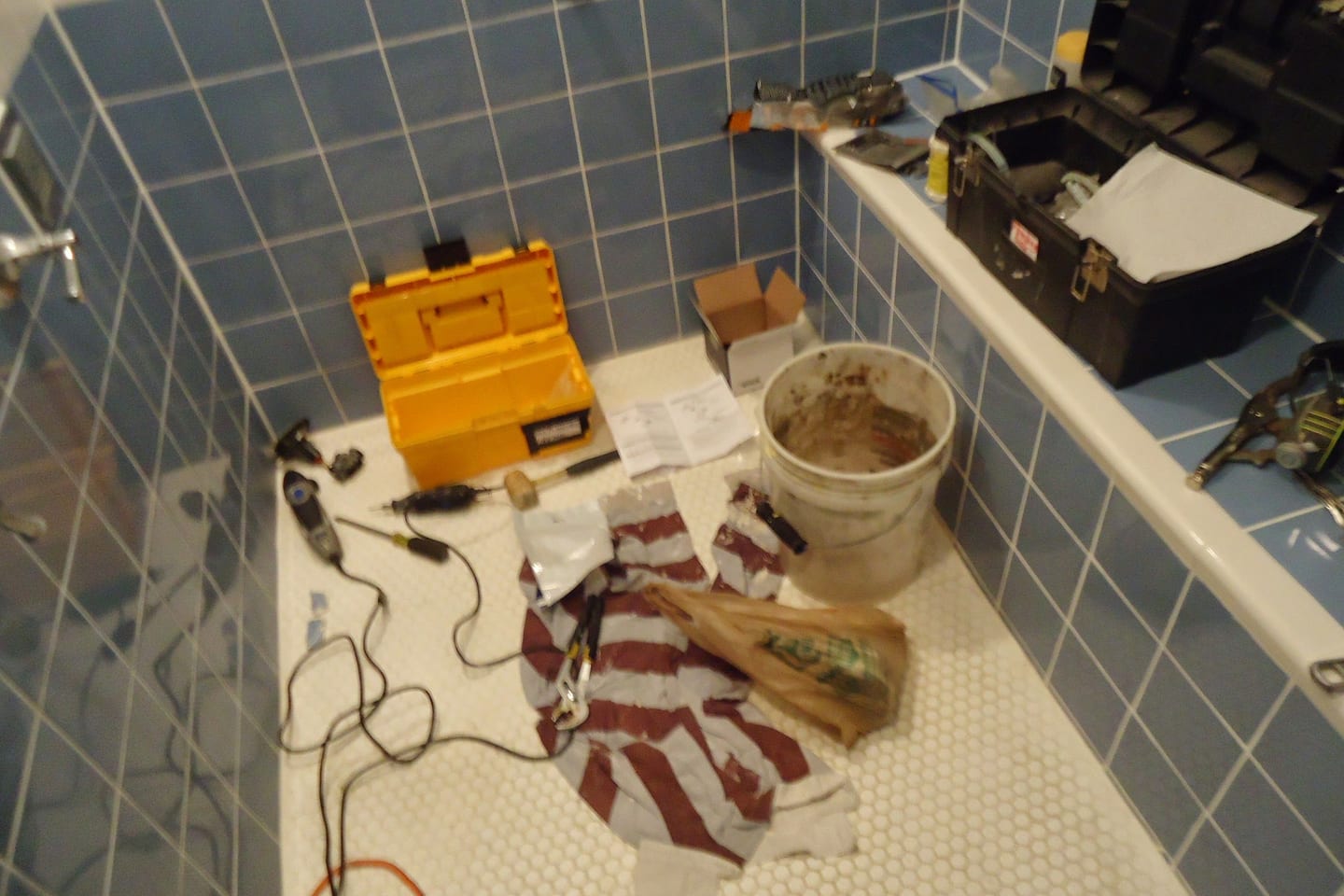 Hand tools laid out on the floor of a shower enclosure beside a mixing valve that has been taken apart
