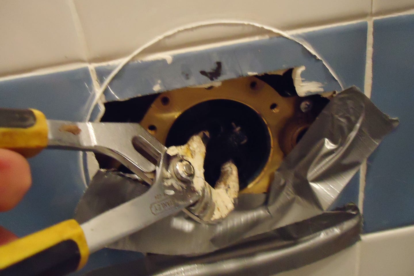 Pliers gripping the retaining clip of a shower valve cartridge in an opened wall recess