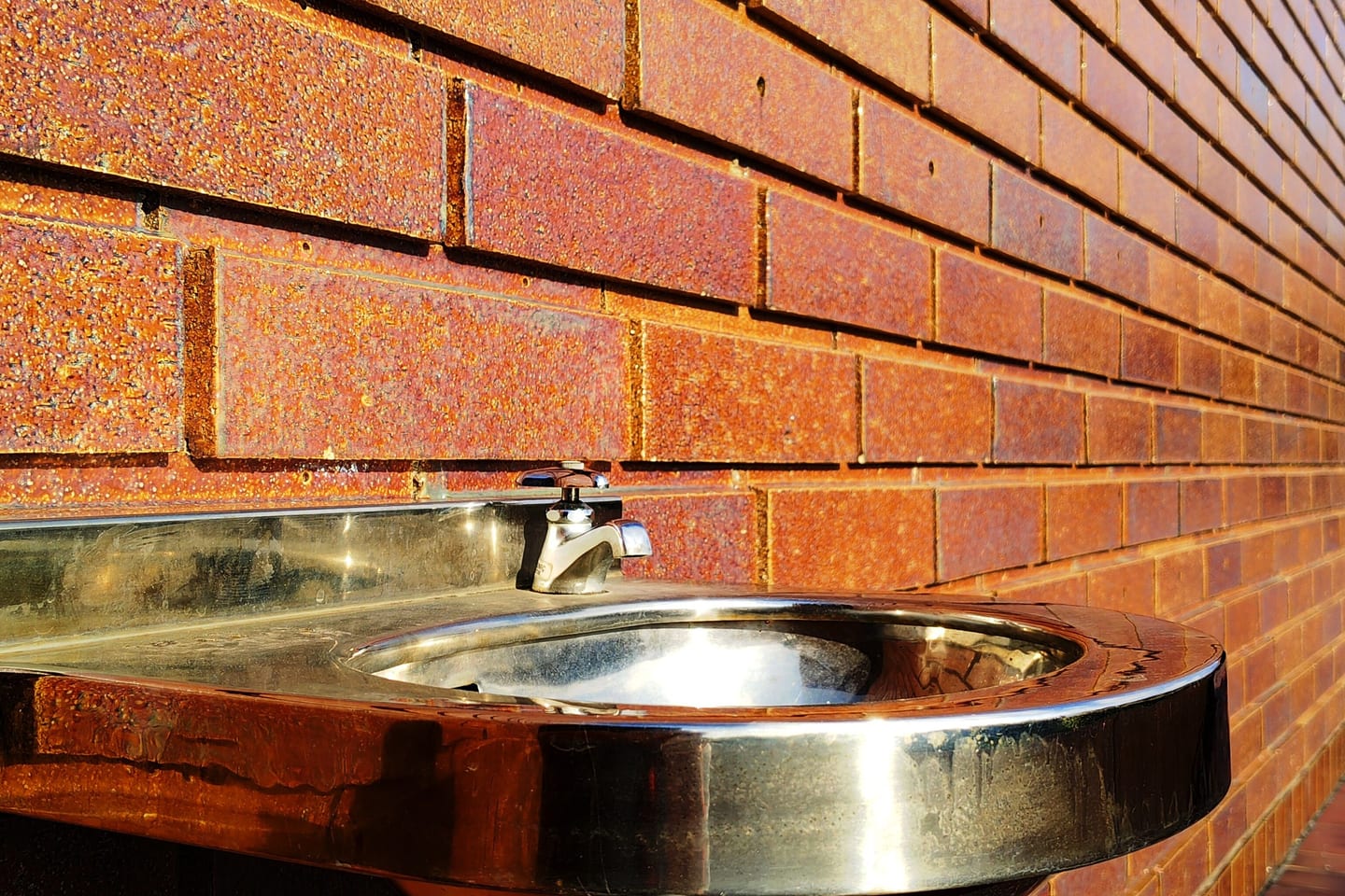 An outdoor utility sink with its waste trap left exposed against a brick wall