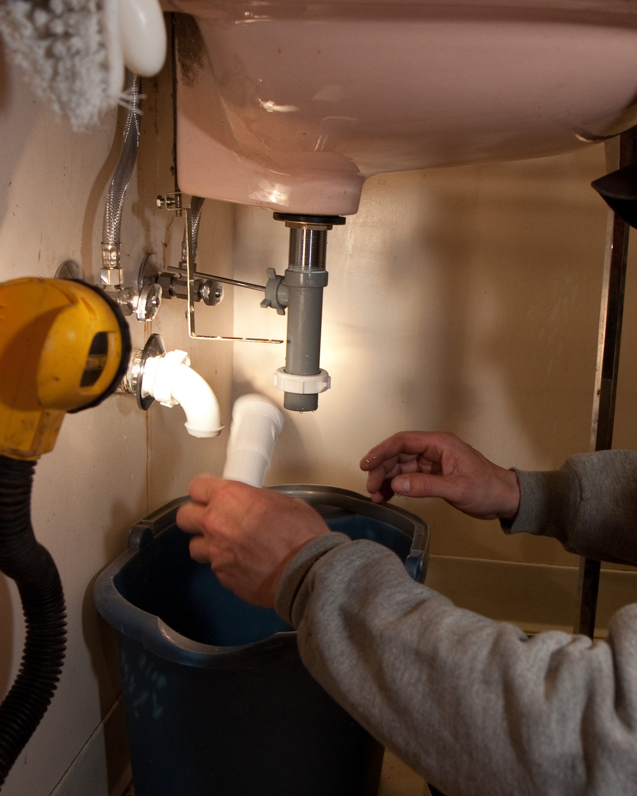 A plumber's hands easing a sink trap apart over a bucket set to catch the water