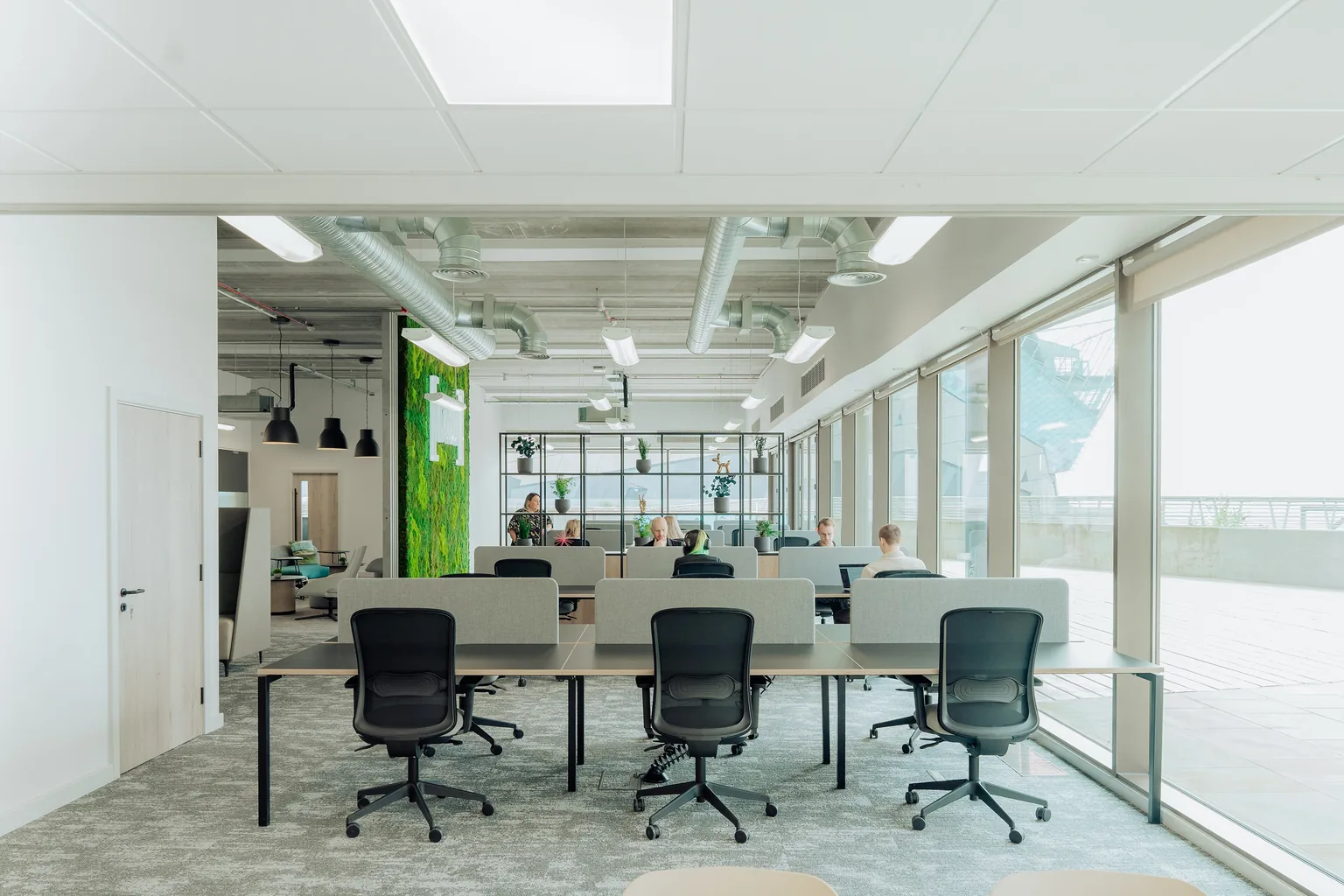 An open-plan office floor with desk pods, task chairs and a planted divider