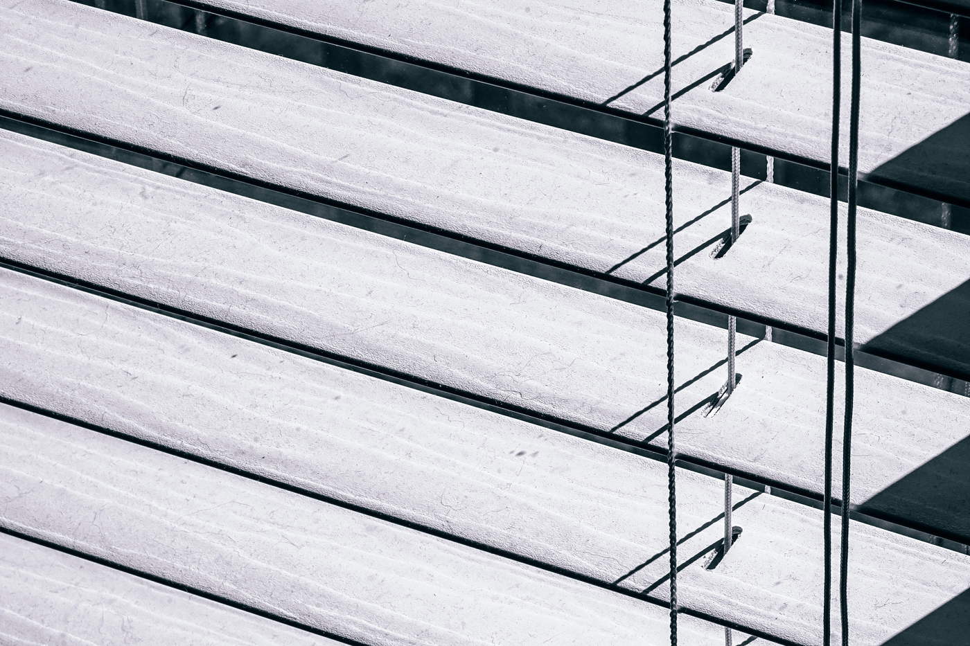 A close view of open venetian blinds, the horizontal slats casting parallel bands of light and shadow.