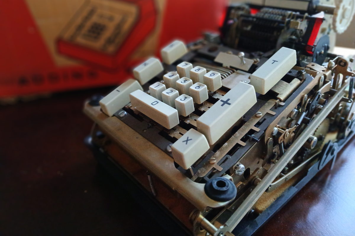 A mechanical adding machine on a desk, its numbered keys and plus bar in the foreground and the type bars behind.