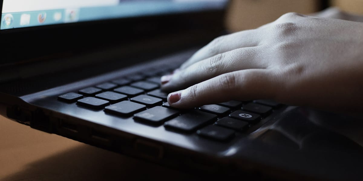 A hand resting on a dark laptop keyboard in low light.