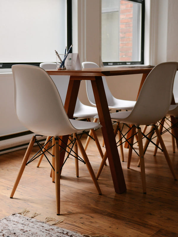 A wooden meeting table ringed by moulded chairs in front of a window