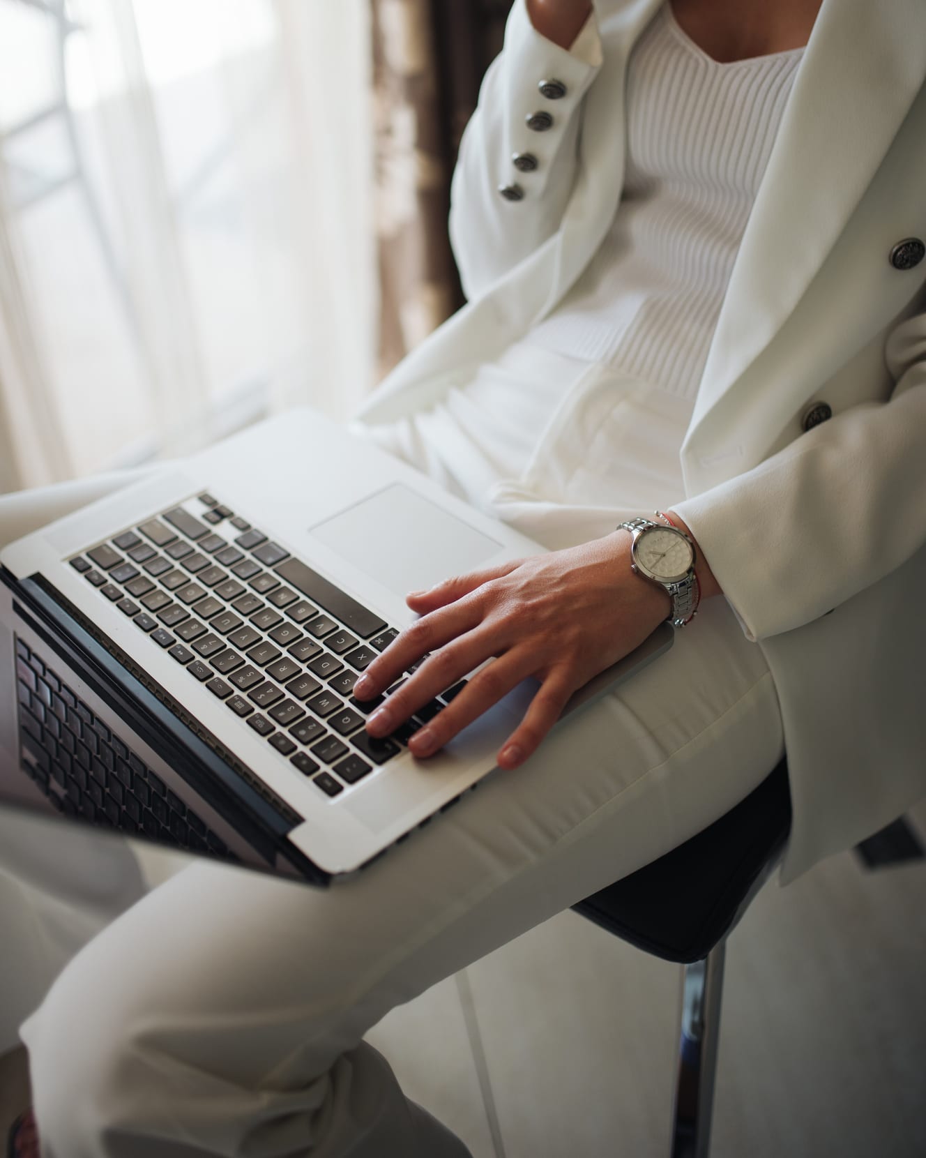 A professional working on a laptop in a bright office, cropped below the face.