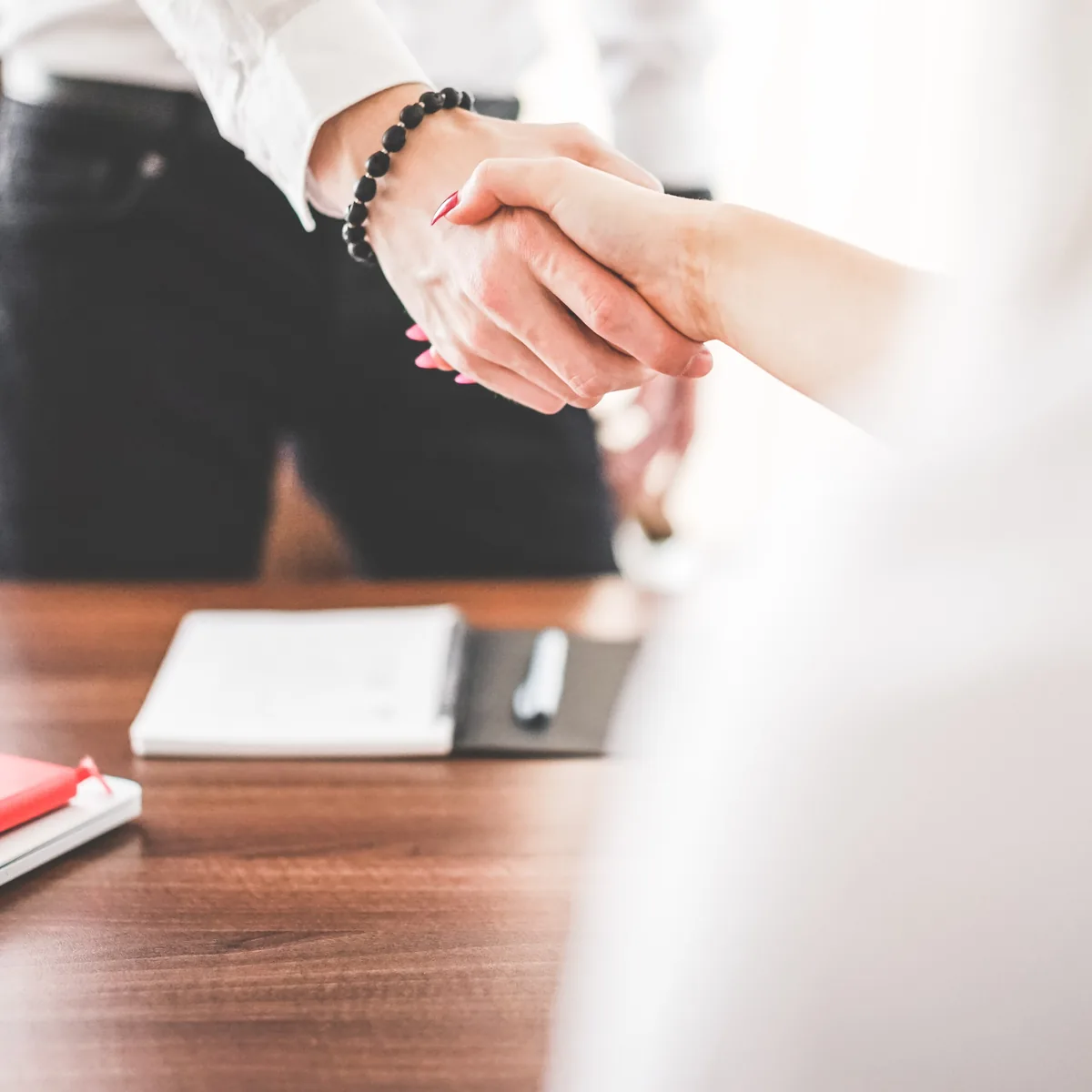 Two people shaking hands across a desk at the end of a meeting
