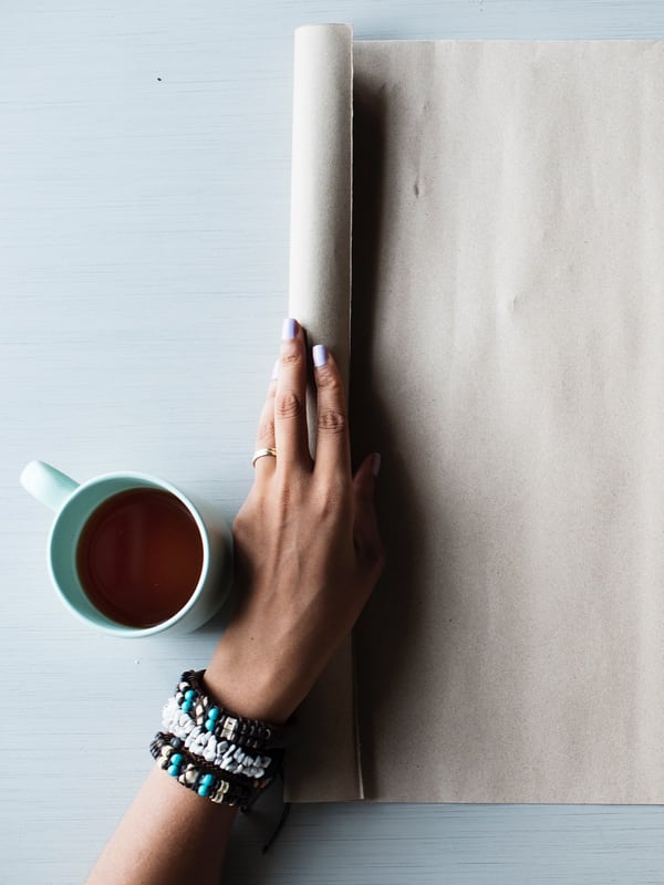 A hand holding a blank sheet of paper open on a table beside a mug of tea