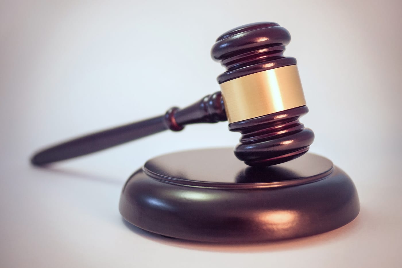 A dark wooden gavel with a brass band resting on its block against a pale background.