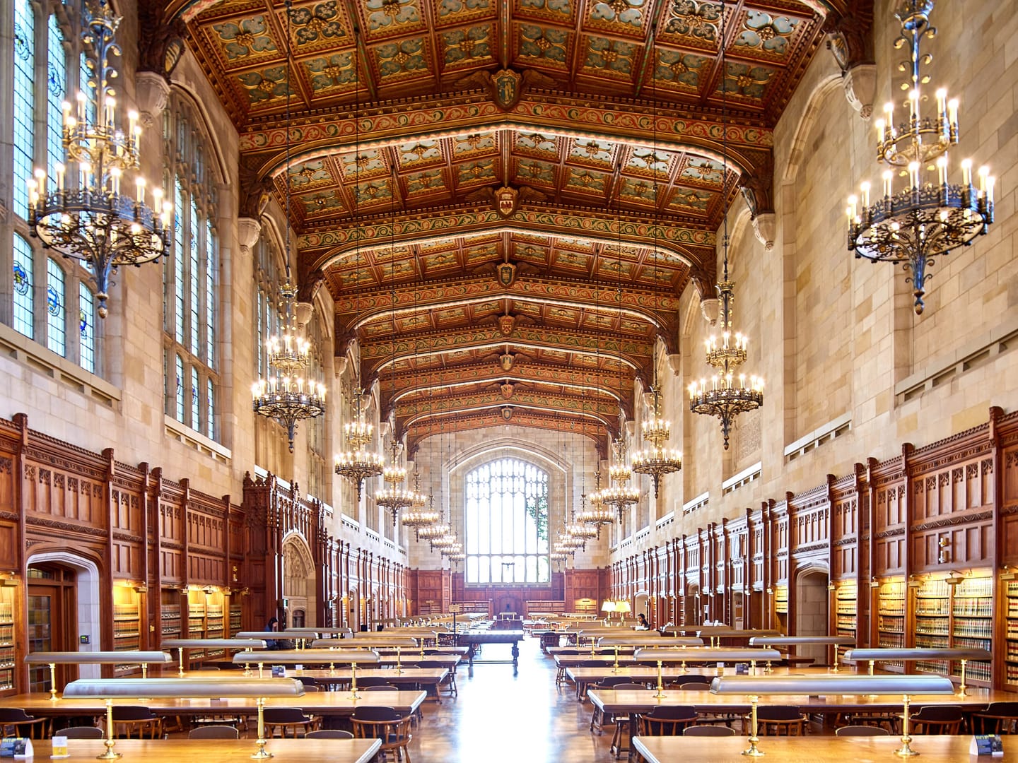 A long law library reading room with wooden tables under chandeliers and a painted vaulted ceiling.