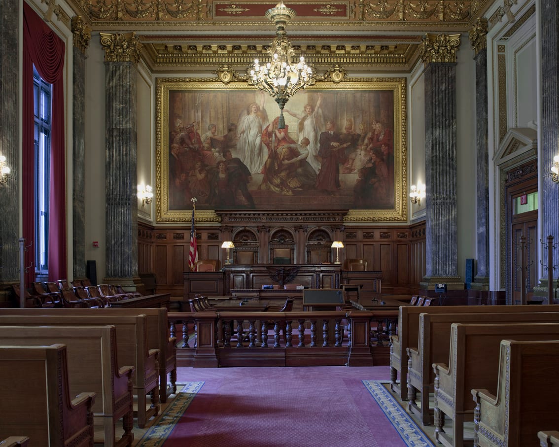 An empty courtroom photographed from the public seating, with a raised bench and panelled walls.