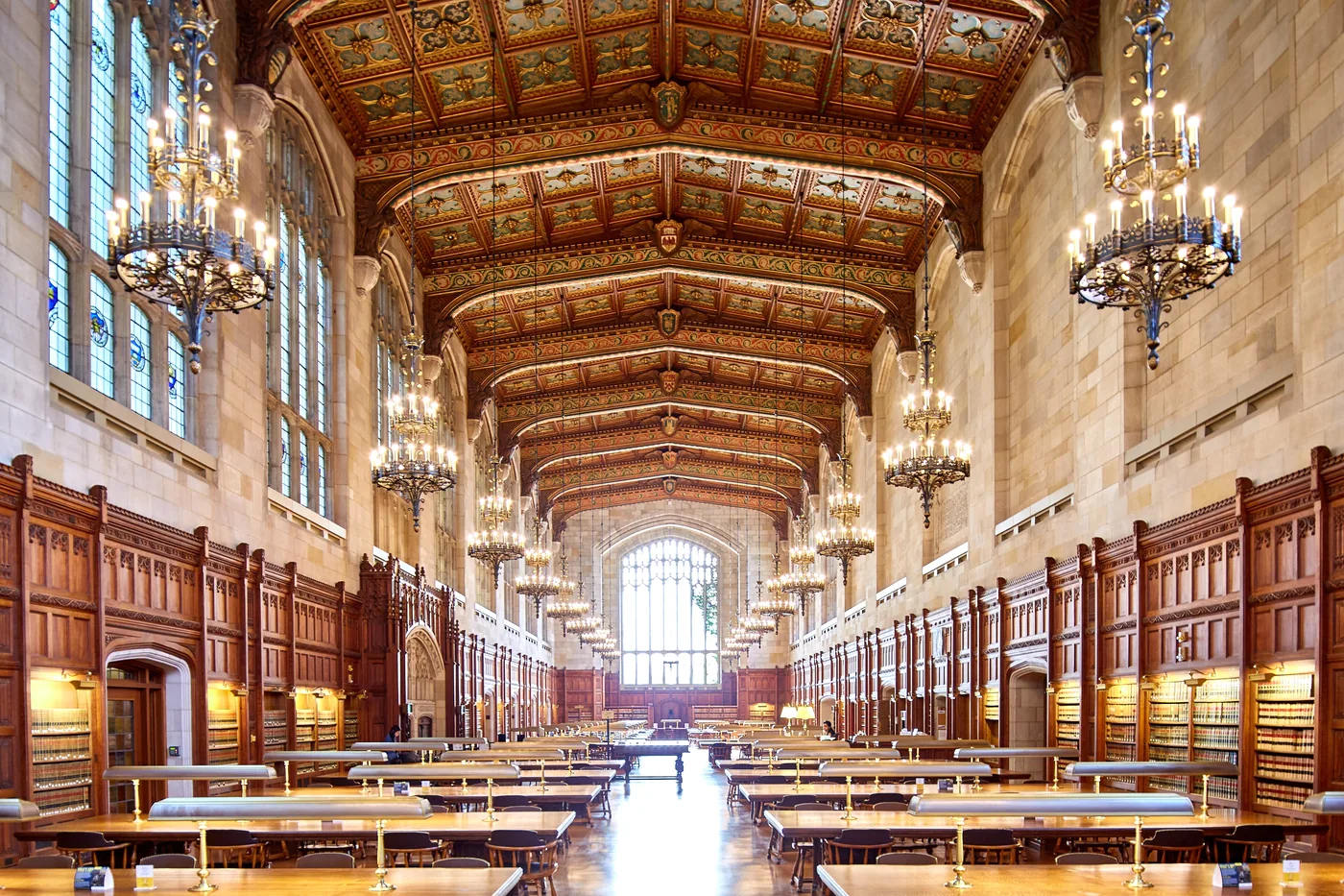 A law library reading room with long study tables, hanging lamps and shelved case reporters along the walls.