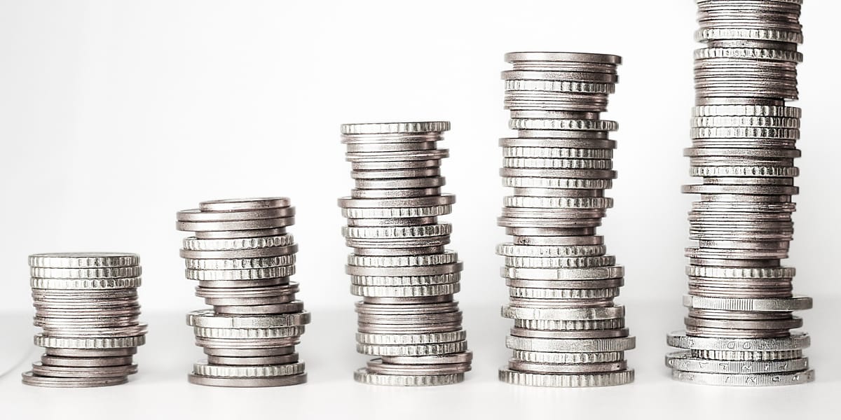 Five stacks of silver coins of increasing height standing in a row on a white surface.