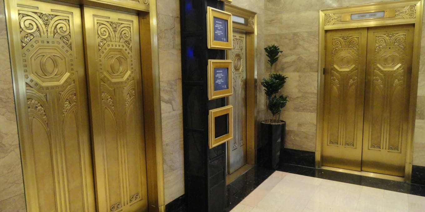 Polished brass lift doors set into a marble lobby wall, lit from above.
