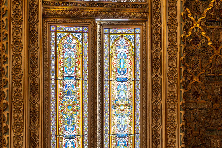 A gilded interior door with leaded coloured glass panels, photographed against dark panelling.