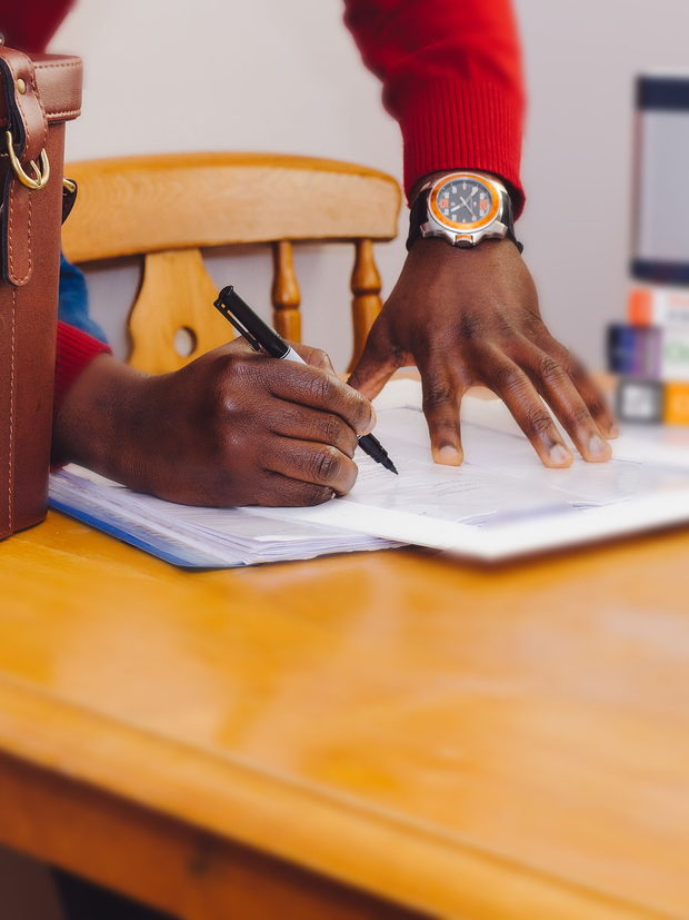 A person writing on a form at a wooden table, cropped below the shoulders so no face is visible.