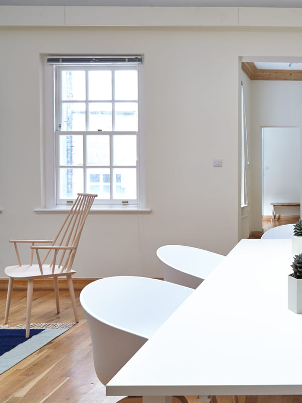 A calm white meeting room with a long table, chairs and a blank board