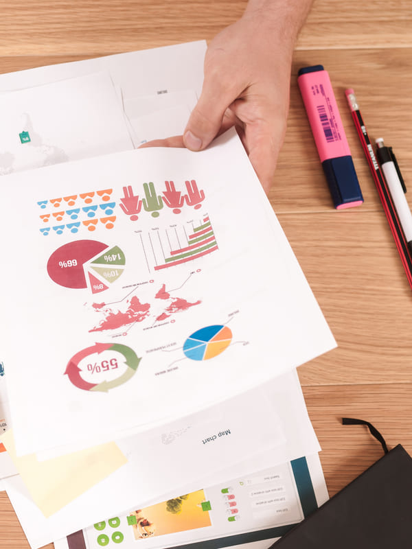 Hands laying out printed charts and summary pages across a desk, highlighter and pencil alongside