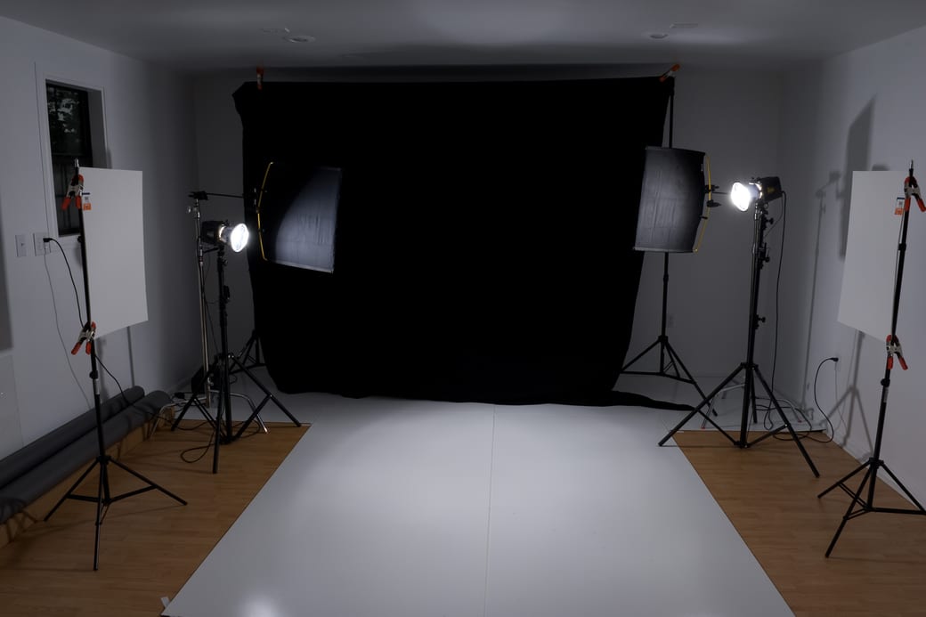 A black studio backdrop flanked by two softboxes on stands above a swept white floor.