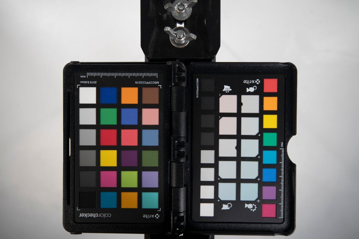 Two colour checker charts held open on a stand against a plain grey ground.