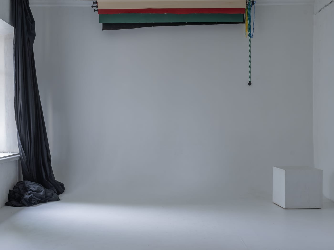 A grey cyclorama wall with rolled paper backdrops on a ceiling rail and a white cube seat to one side.
