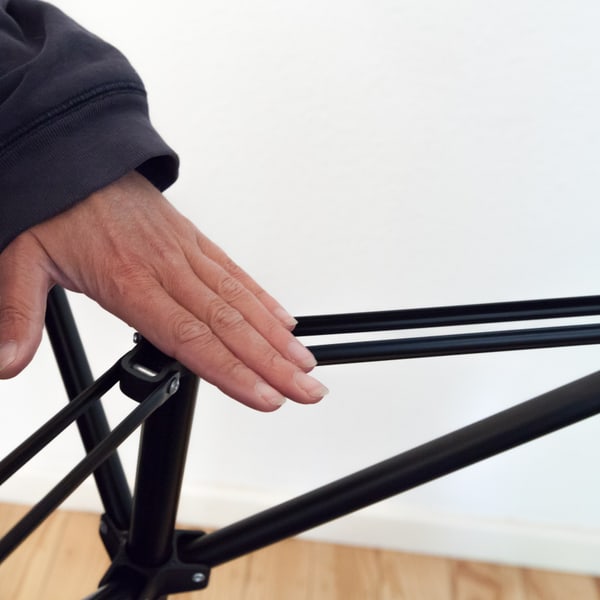 A hand running along the folded braces of a light stand as it is opened out
