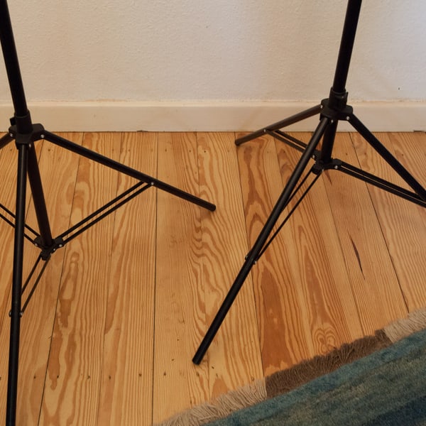 The braced legs of two light stands planted on a studio floor