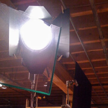 A studio lamp burning behind its barn doors, a diffusion frame swung in front of it and a black flag on a second C-stand