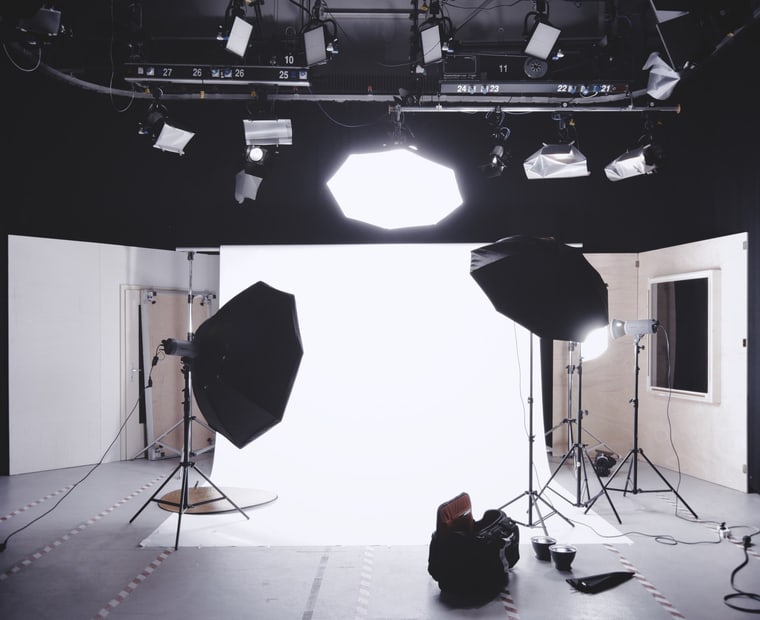 An empty shooting floor: white cyclorama wall, octaboxes and an umbrella on stands under an overhead lighting grid