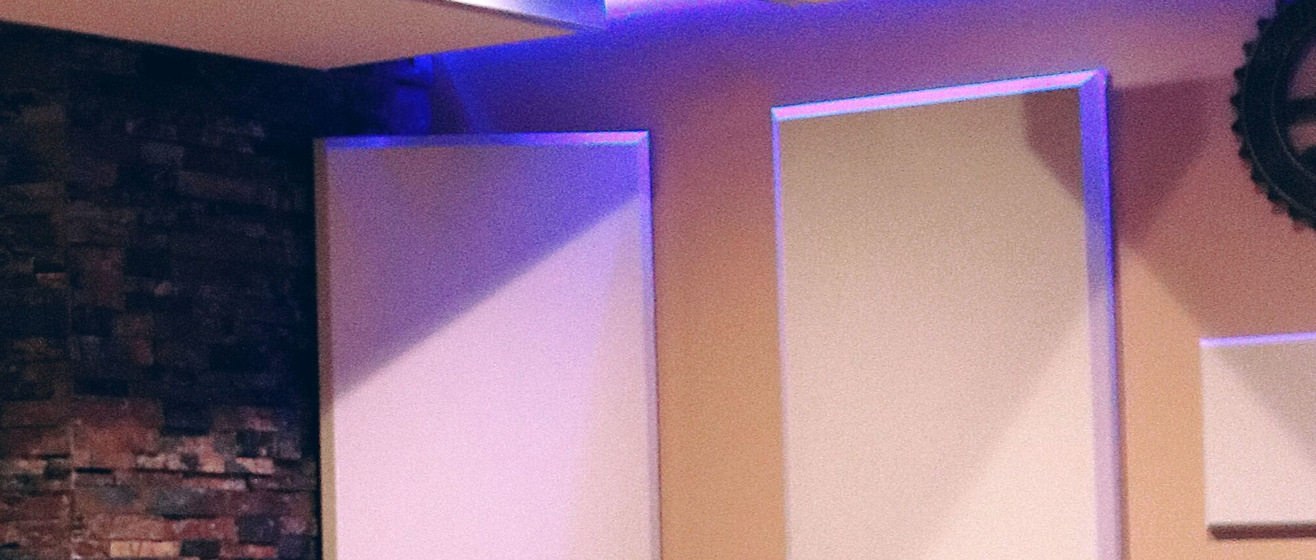 A brick wall lined with cream acoustic panels, their edges lit in purple.